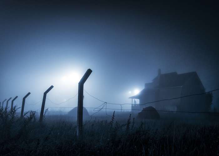 spooky looking farm house in the distance in a foggy field at night