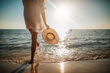 woman holding hat standing in surf at sunset