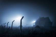spooky looking farm house in the distance in a foggy field at night