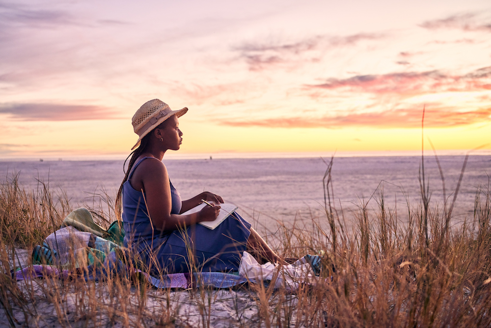 young woman journaling on the beach at sunset